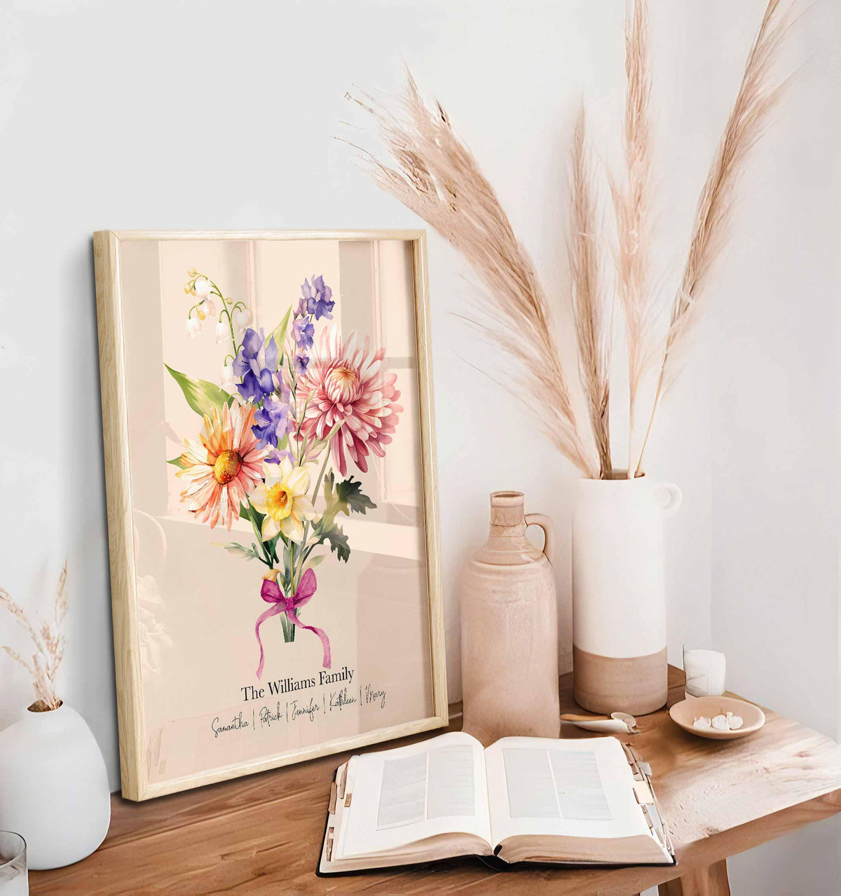 Personalized family bouquet print in an oak frame on a wooden desk with pampas grass and an open book