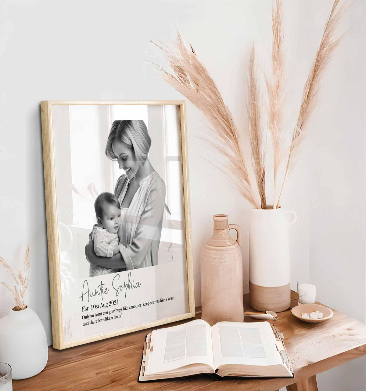 Personalized auntie print in a light oak frame on a wooden desk beside pampas grass and an open book