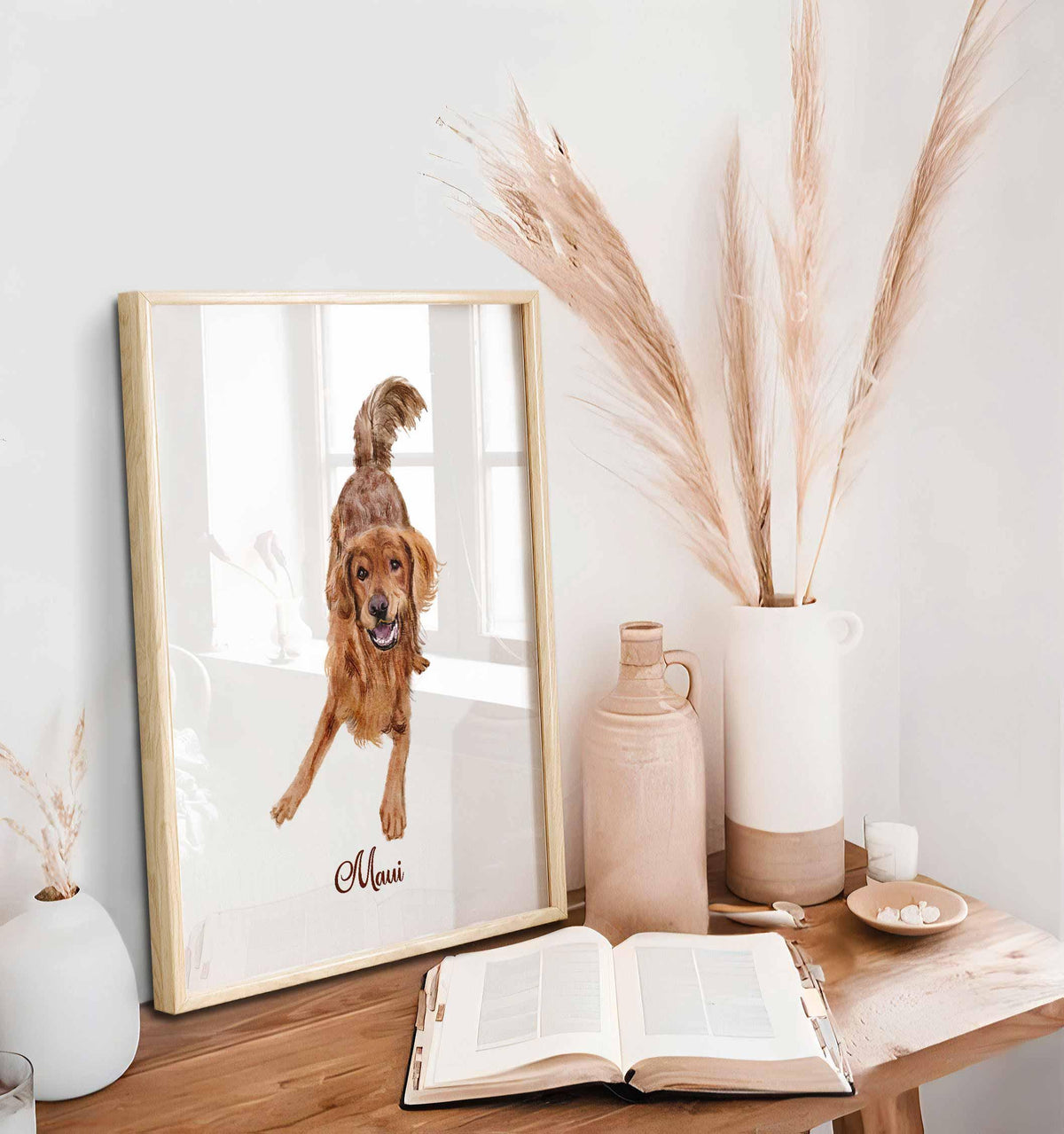 Framed pet portrait of a golden retriever named Maui on a desk with pampas grass and an open book